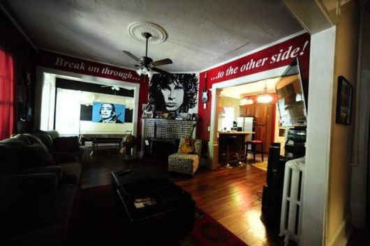 Sala de estar ampla com instrumentos musicais dispostos ao longo de sua extensão e paredes personalizadas com um quadro do The Doors e os dizeres "Break on through the other side!"