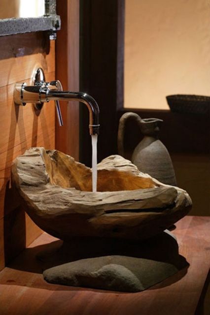 Foto de uma torneira de lavabo aberta com a água caindo em uma cuba feita de madeira. 