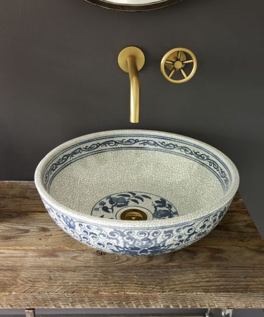 Torneira de lavabo dourada com uma abertura circular e cuba de cerâmica. 