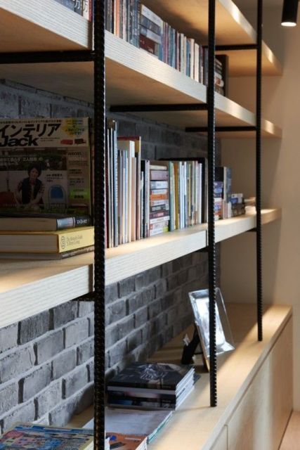 Foto de uma estante com vigas de ferro aparentes e bases de madeira onde estão posicionados livros e quadros.  Ela vai de uma extremidade lateral da parede à outra. 