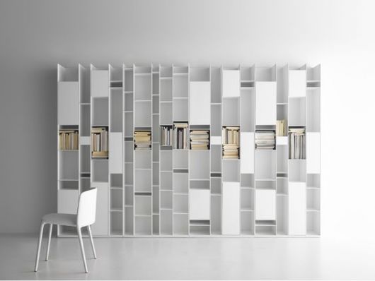 Ambiente vazio completamente branco com uma prateleira em design futurista de MDF e livros posicionados em algumas de suas aberturas. 