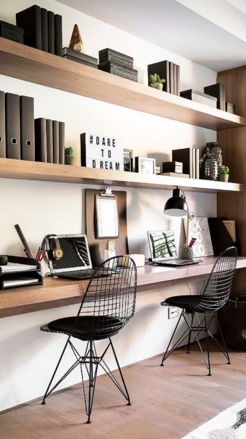 Três estantes paralelas na parede com livros, notebook e objetos de decoração nelas. Há duas cadeiras em frente à estante mais baixa. 