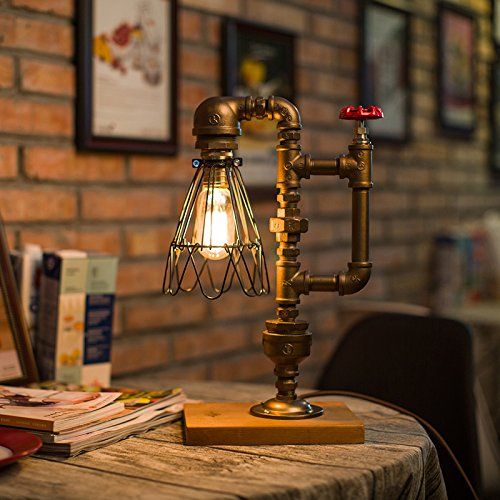 Foto de uma luminária retrô em cima de uma mesa. Seu "corpo' é feito com canos e a extrema tem uma lâmpada. 