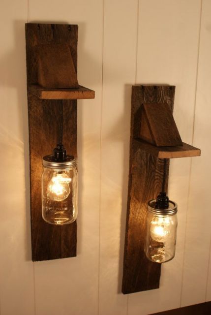 Foto de duas luminárias de parede. As duas são fixadas a uma base de madeira instalada na parede por meio de uma corrente e tem um pote de vidro para cobrir a lâmpada. 