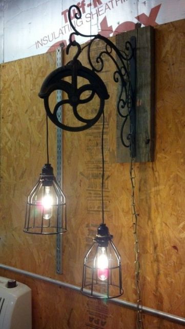 Duas lâmpadas penduradas em uma roldana fixada na parede. As lâmpadas são cobertas por um objeto metálico com certas aberturas em sua dimensão. 