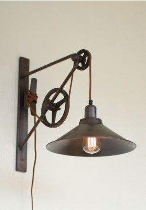 Foto de uma luminária suspensa por meio de corda que a liga em uma roldana pendurada na parede. 