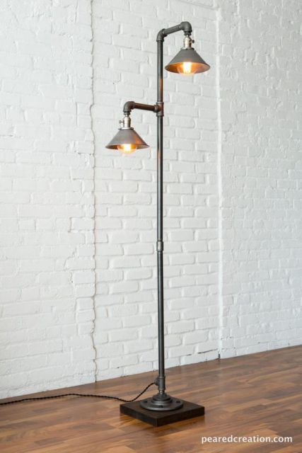 Foto de uma luminária de chão alta com um cano que termina em duas extremidades, cada uma com uma lâmpada protegida por estruturas metálicas que se parecem com chapéus. 