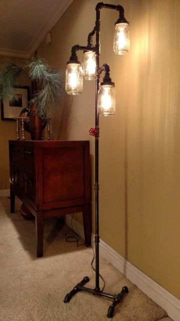 Foto de uma luminária de chão alta com saída para quatro lâmpadas no topo, cada uma delas protegida por vidros. 