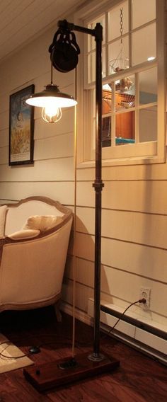 Foto de uma luminária de chão ligada na tomada. Ela é alta e tem uma roldana no topo que sustenta uma lâmpada. 