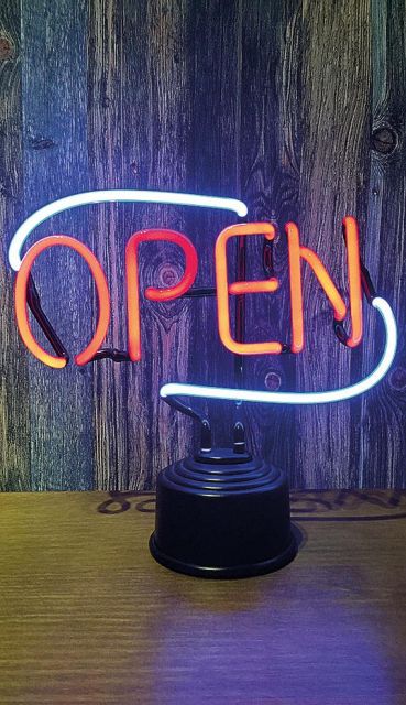 Foto de uma luminária de mesa com letreiro em cores neon escrito "Open".