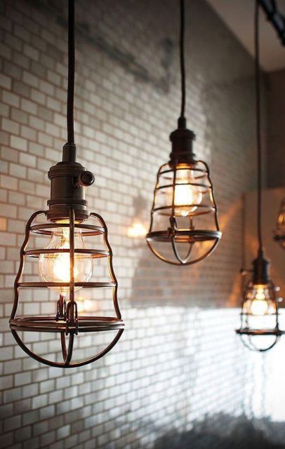 Foto de três luminárias retrô penduradas no teto por fios. As lâmpadas são envoltas por um material metálico que parece uma mini jaula. 