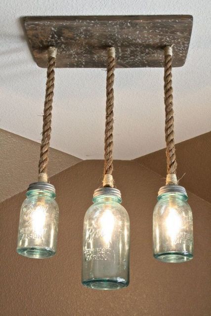 Foto de três lâmpadas ligadas a uma madeira pendurada no teto por uma corda. As lâmpadas são envoltas por recipientes de vidro que parecem potes. 