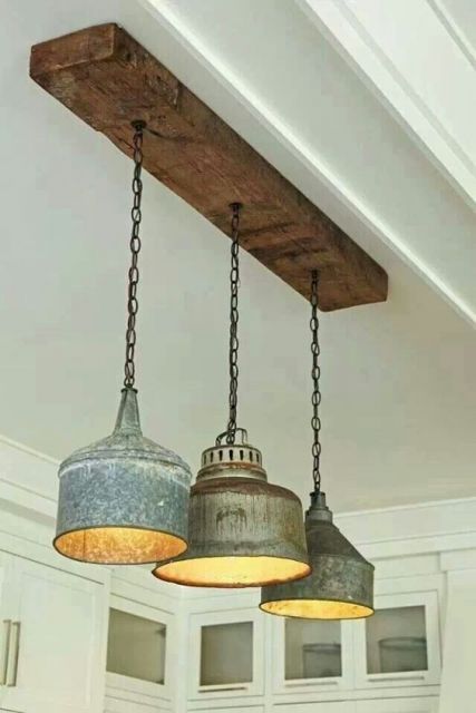 Foto de três lâmpadas ligadas a uma madeira pendurada no teto por uma corrente. as lâmpadas estão dentro de recipientes metálicos grandes e largos. 