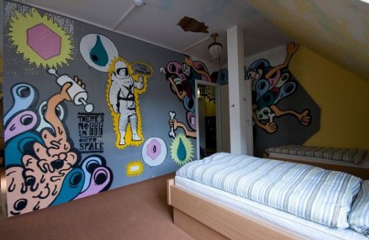 Quarto com duas camas e na frente delas uma parede grafitada com desenhos variados. 