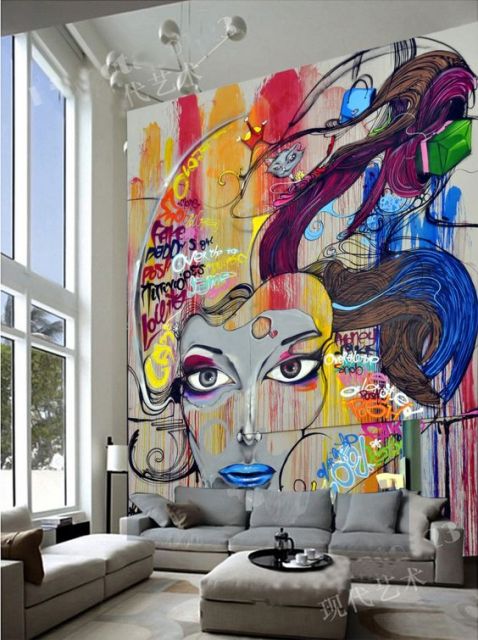 Foto de uma sala com paredes muito altas. Na parede atrás do sofá há um grafite colorido com o rosto de uma mulher. 