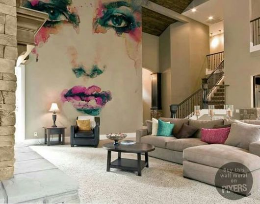 Sala ampla com móveis espaçados. Em uma parede lateral há o grafite do rosto de uma mulher feito com cores vivas. 