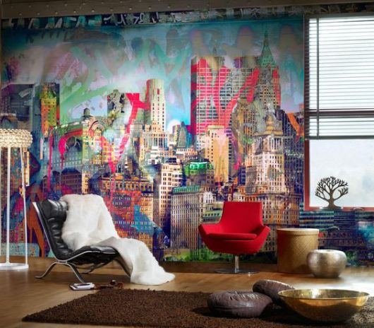 Foto de um ambiente com tapete e algumas poltronas. Atrás deles há uma parede grafitada com os prédios de uma metrópole. 