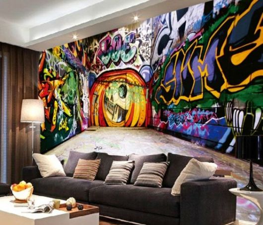 Foto de uma sala onde na parede atrás do sofá há um grafite tridimensional com muitas cores e letras. 
