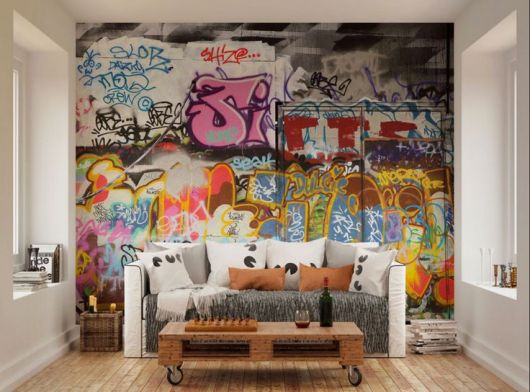 Foto de uma sala pequena com um sofá e uma mesa de centro. Atrás do sofá há uma parede colorida com grafite. 