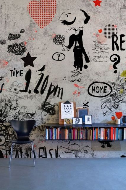 Foto de uma parede onde há uma cadeira e uma estante de livros. Na parede há diversos desenhos grafitados. 