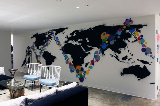 Foto de um ambiente social da casa com sofá e cadeira onde há uma parede grafitada com o mapa mundi. 