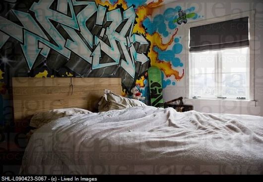 Foto de uma cama com cabeceira de pallets e a parede atrás dela toda decorada com grafite, principalmente letras. 