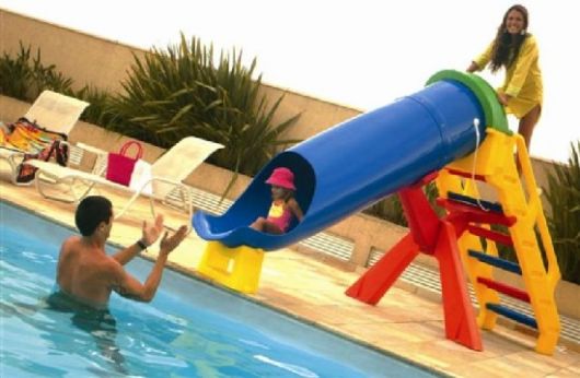 Criança escorregando em uma escorregador de piscina de plástico colorido com seu pai dentro da piscina esperando para recebê-la. 
