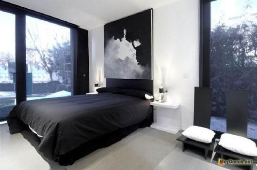 A cama com colcha preta se destaca em meio às paredes em branco