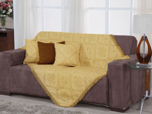 sofá marrom com manta amarela e almofadas.