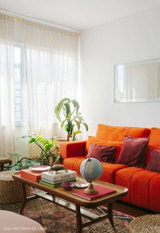 1 sala com sofa laranja e parede branca