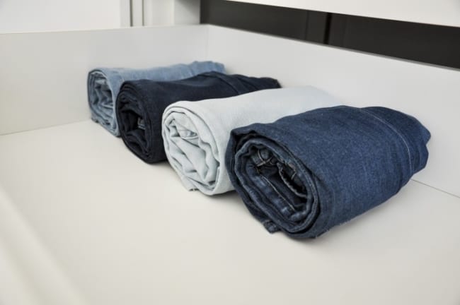 quatro calcas jeans de tons diferentes dobradas em rolo dentro de uma prateleira no armario